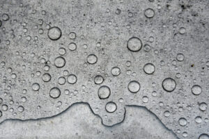 Close-up of water drops on a rough surface showing water-repelling behavior.