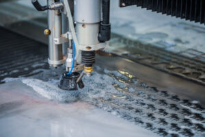 Waterjet cutter shaping material with water spraying around the cutting head.